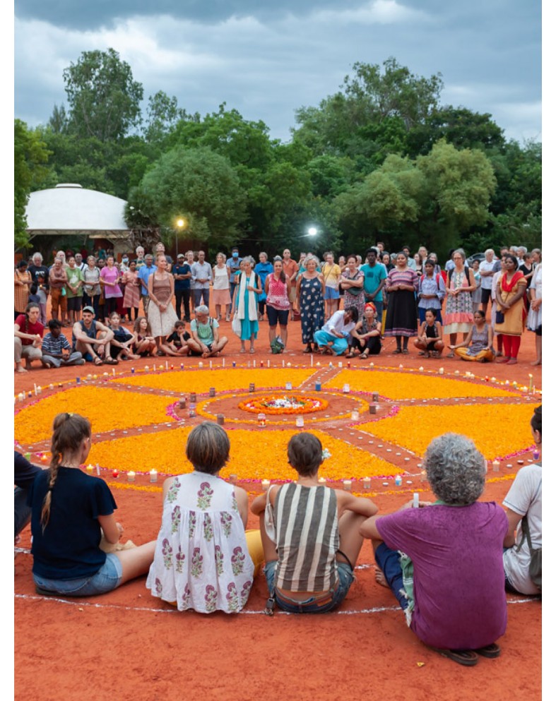 Auroville community gathered around a circular flower arrangement